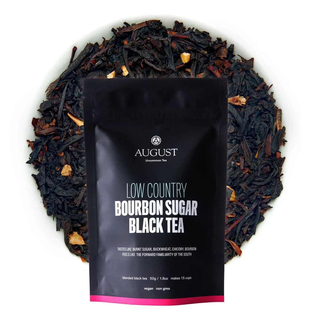 A black pouch of Low Country Bourbon Sugar Black Tea resting on a bed of dried loose tea leaves