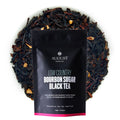 A black pouch of Low Country Bourbon Sugar Black Tea resting on a bed of dried loose tea leaves