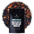 A pouch of Painted Desert black tea surrounded by loose tea leaves containing dried chili, cacao shells, and cinnamon.