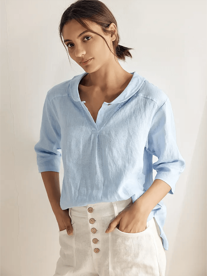 A woman wearing a relaxed-fit linen V-neck top in light blue with half sleeves and an asymmetrical hem.