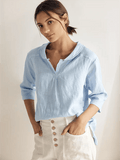 A woman wearing a relaxed-fit linen V-neck top in light blue with half sleeves and an asymmetrical hem.