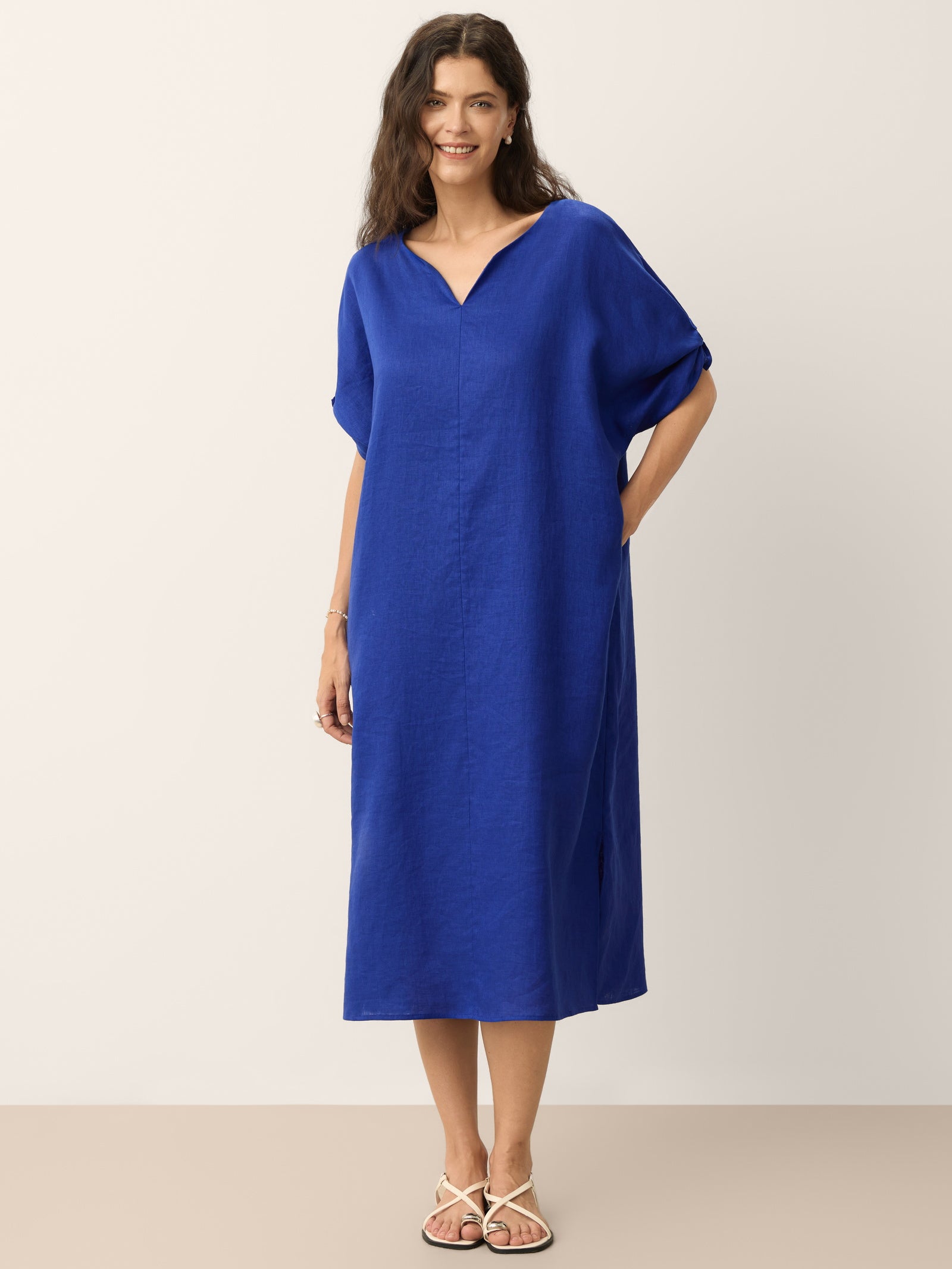 A woman wearing a 100% linen midi dress in a straight silhouette with bow-tie cuff details and side-slit hem.