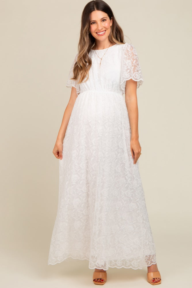 Pregnant woman wearing a white lace flutter sleeve maternity maxi dress with a sheer lace back detail