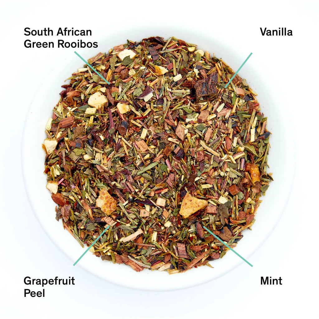 A pouch of Cocteau tea blend next to a small white bowl filled with loose leaf rooibos, grapefruit peel, and mint.