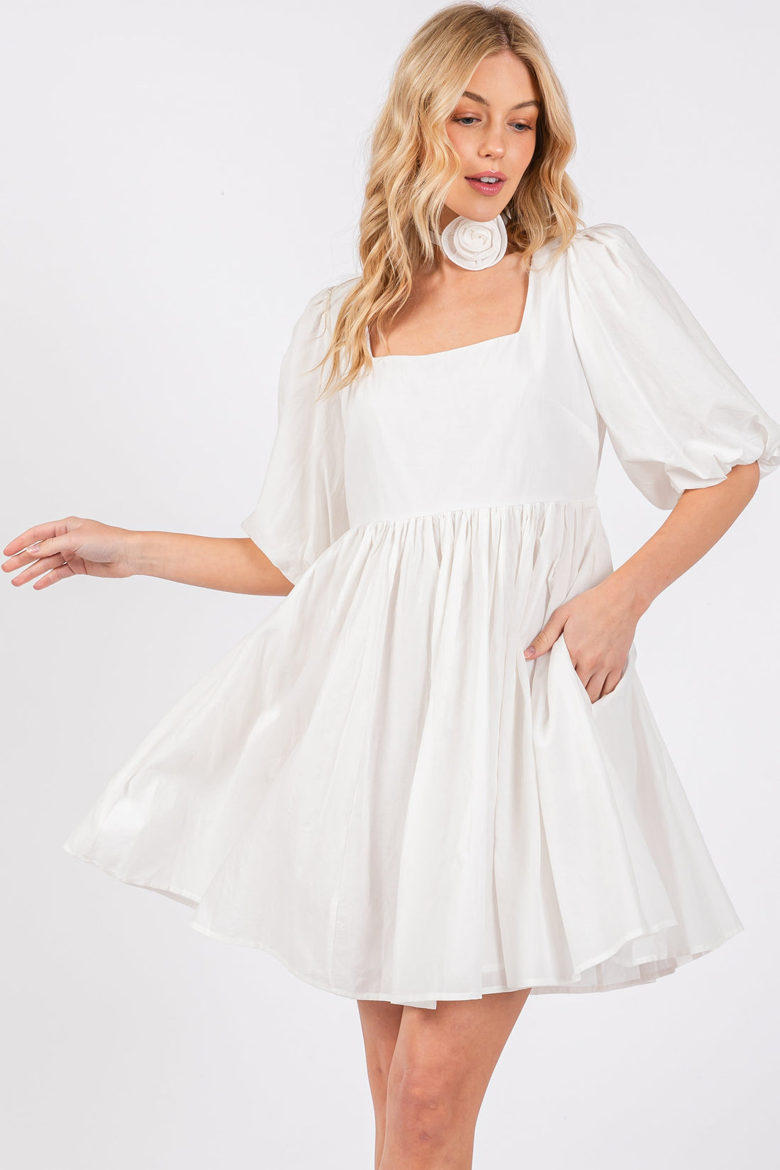 A woman wearing a white square neck babydoll mini dress with puff sleeves and side pockets.