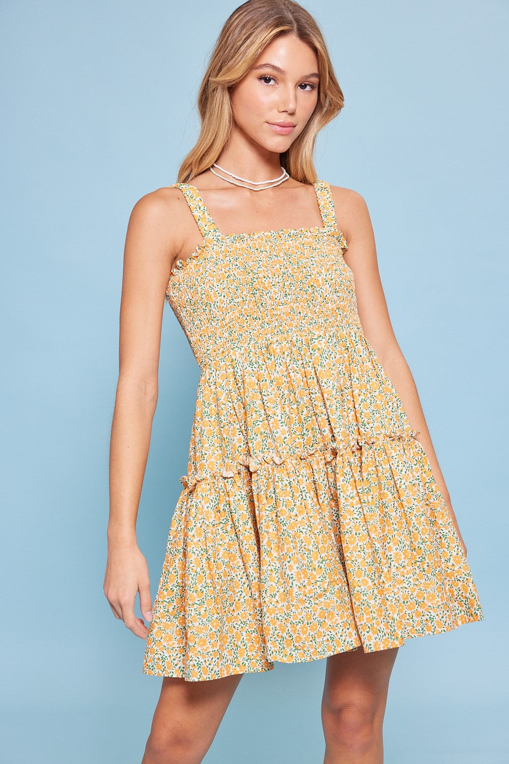 A woman wearing a White Orange Floral Print Smocked Ruffle Mini Babydoll Dress against a light blue background.