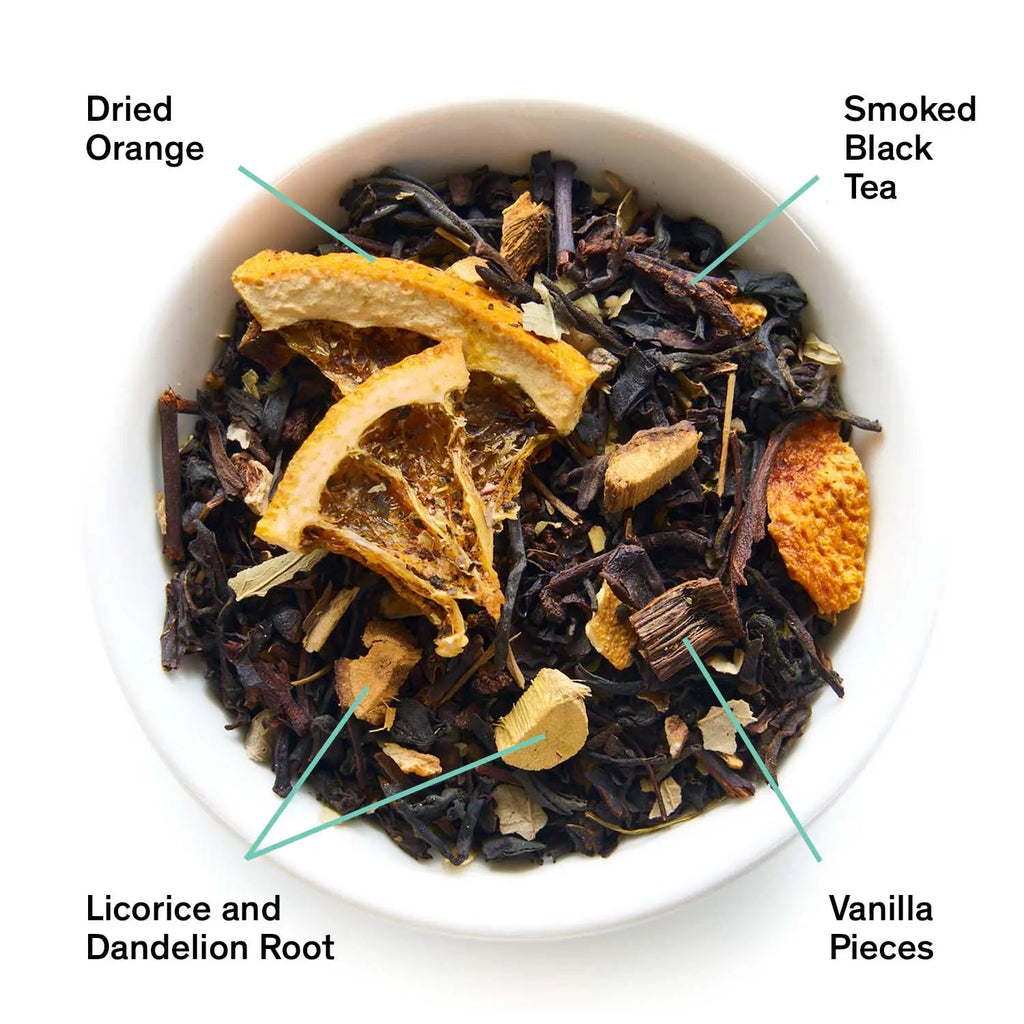 Close up overhead view of Mood Indigo black tea featuring visible dried orange slices, black tea leaves, and vanilla pieces in a small white bowl.
