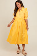 A smiling woman wearing a bright yellow maternity midi dress with short puff sleeves, a collar, and a half-zip front closure.