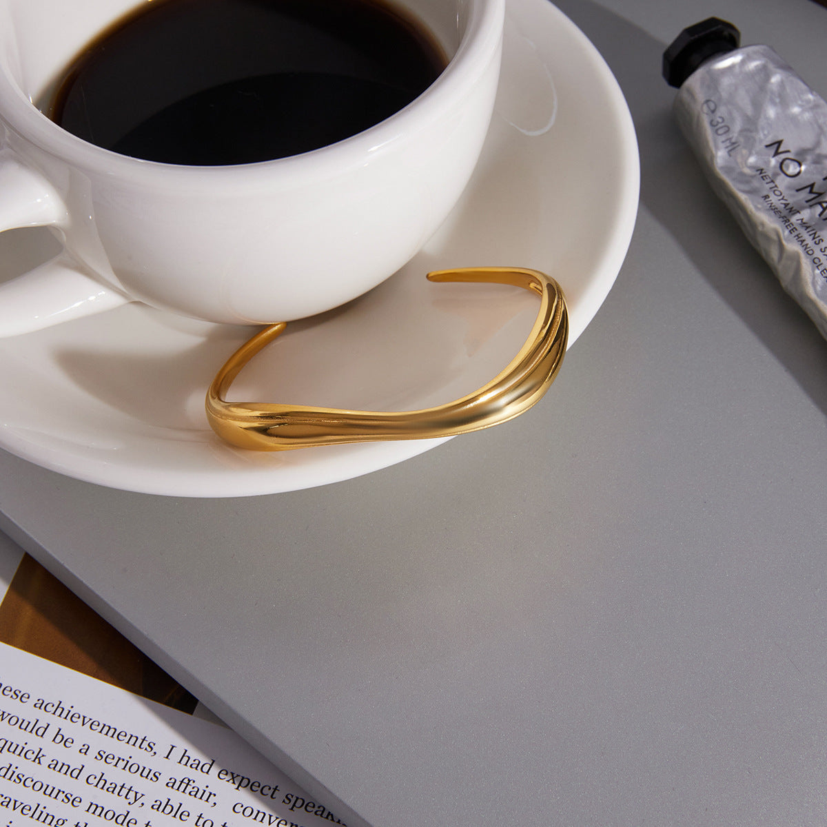 Polished Gold Wave Open Cuff Bracelet in stainless steel resting on a neutral background