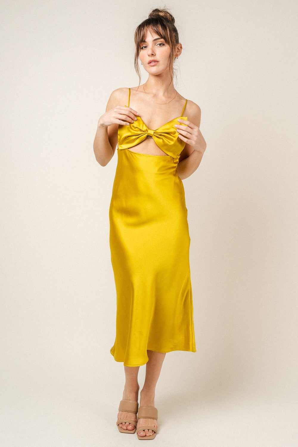 A woman wearing a vibrant yellow satin midi dress featuring a bow detail at the chest and a cut-out midriff, photographed from the front and back against a neutral background.