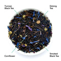 Black Metallic loose leaf tea blend with black tea leaves, oolong, cornflower petals, and elderberry in a white bowl next to a matte black product pouch.