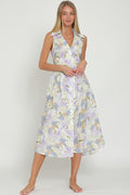 A woman wearing a white and light blue floral sleeveless midi dress with a collar, button-down front, and tie-back detail.