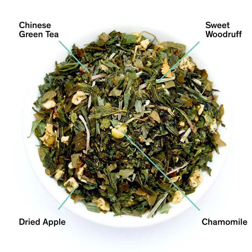 Neon Forest green tea blend with chamomile, dried apple, and sweet woodruff in a white bowl next to black product packaging.