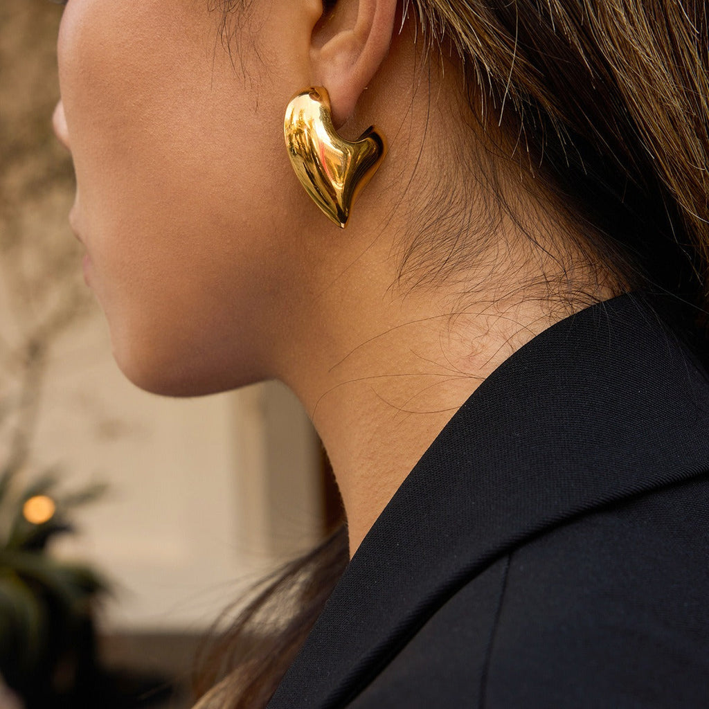 A pair of elegant 18K gold-toned heart-shaped titanium steel stud earrings against a neutral background.