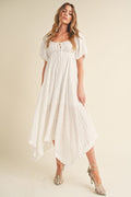 A model standing wearing a white flowy midi dress with puff sleeves and a tie-front detail against a neutral studio background.