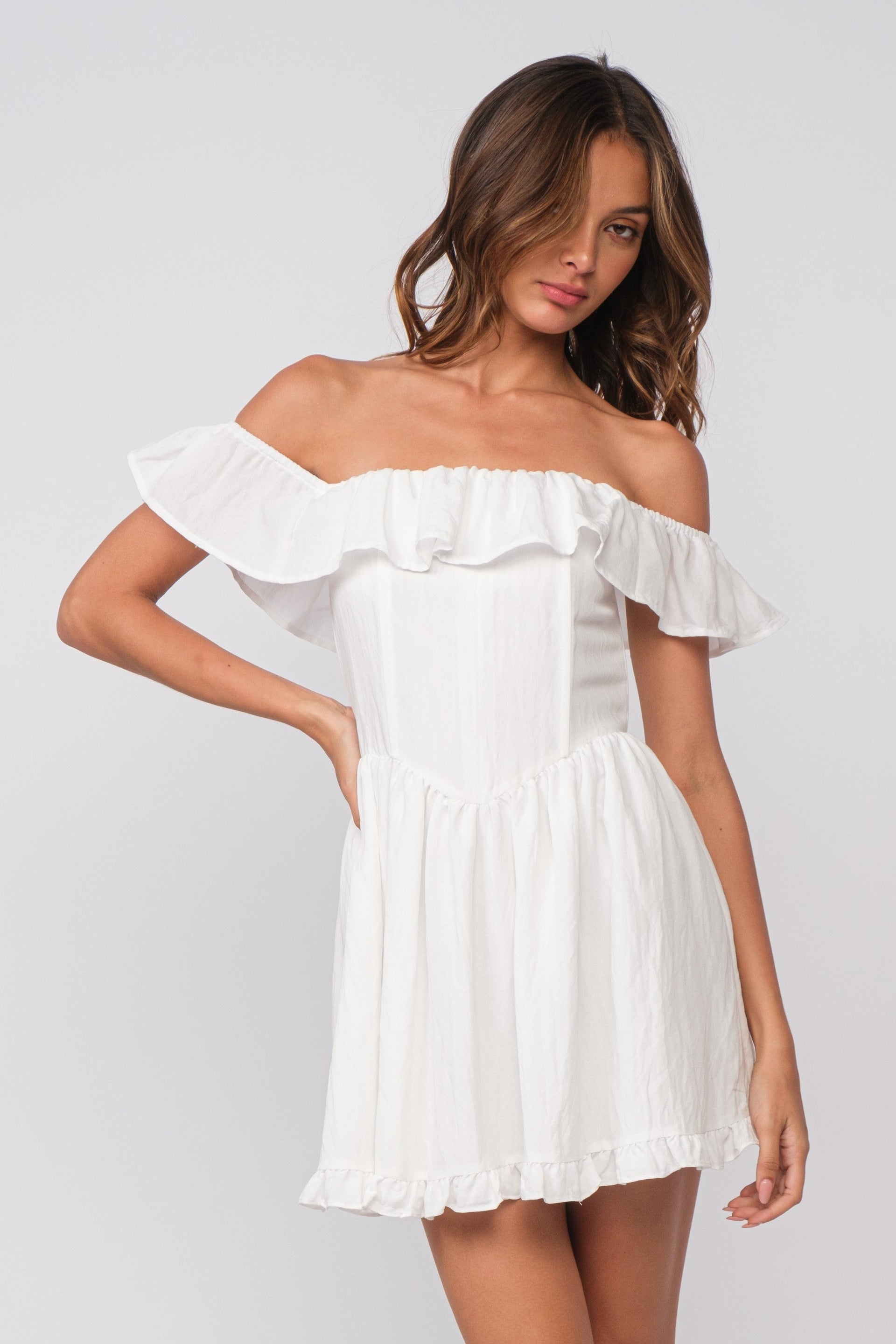 A woman wearing a white off-shoulder mini dress with ruffled details and a drop-waist silhouette.