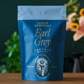 Organic Earl Grey black tea loose leaves in a bowl with cornflower petals, labeled 'Essentials Earl Grey'.