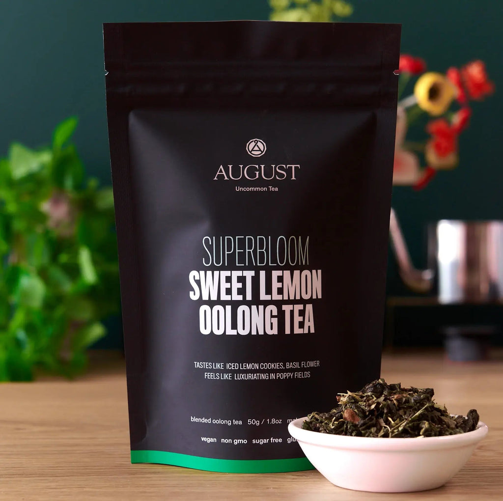Bag of Superbloom Sweet Lemon Oolong Green Tea next to a small bowl of dry tea leaves including lemon verbena and marigold flowers.