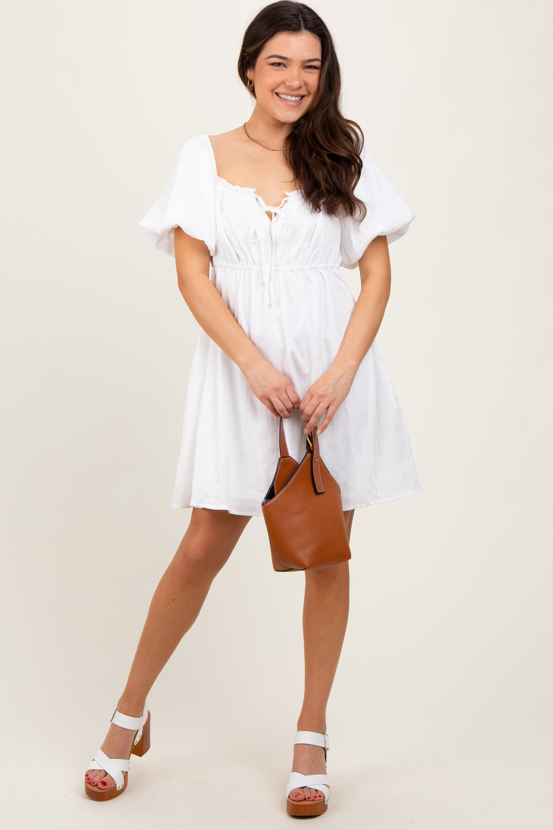 A pregnant woman wearing a white short-sleeve mini dress with bubble sleeves and a textured fabric, styled with tan sandals.