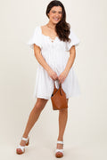 A pregnant woman wearing a white short-sleeve mini dress with bubble sleeves and a textured fabric, styled with tan sandals.