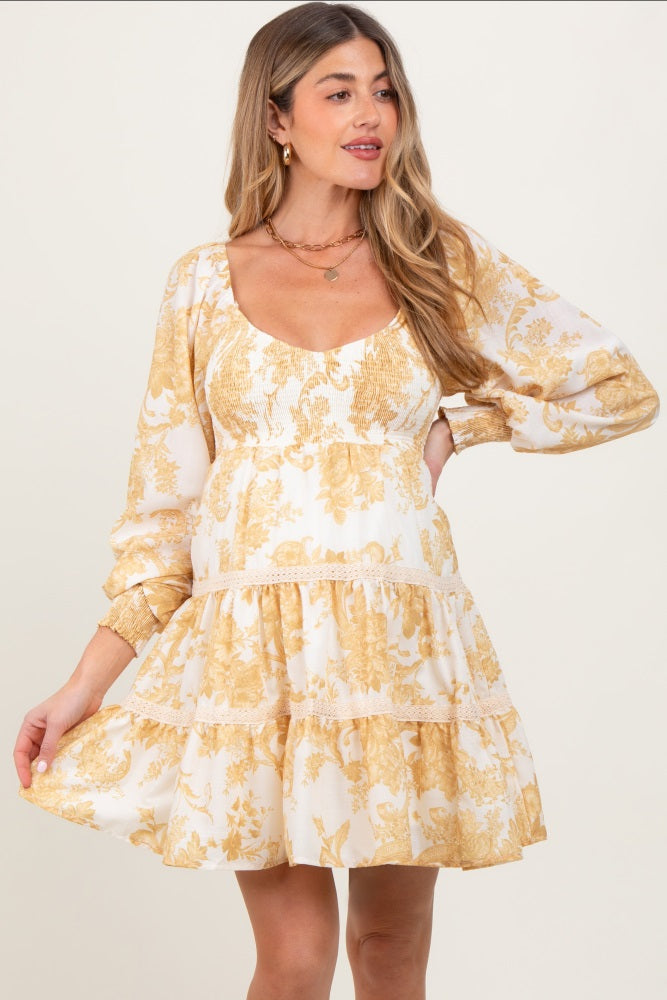 A pregnant woman wearing a yellow floral smocked bubble sleeve tiered maternity dress