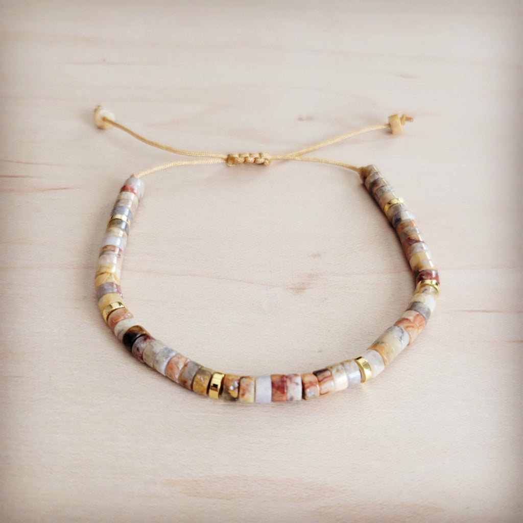 Close up of an adjustable Aqua Terra stone bead bracelet with gold-tone accents on a light wooden background