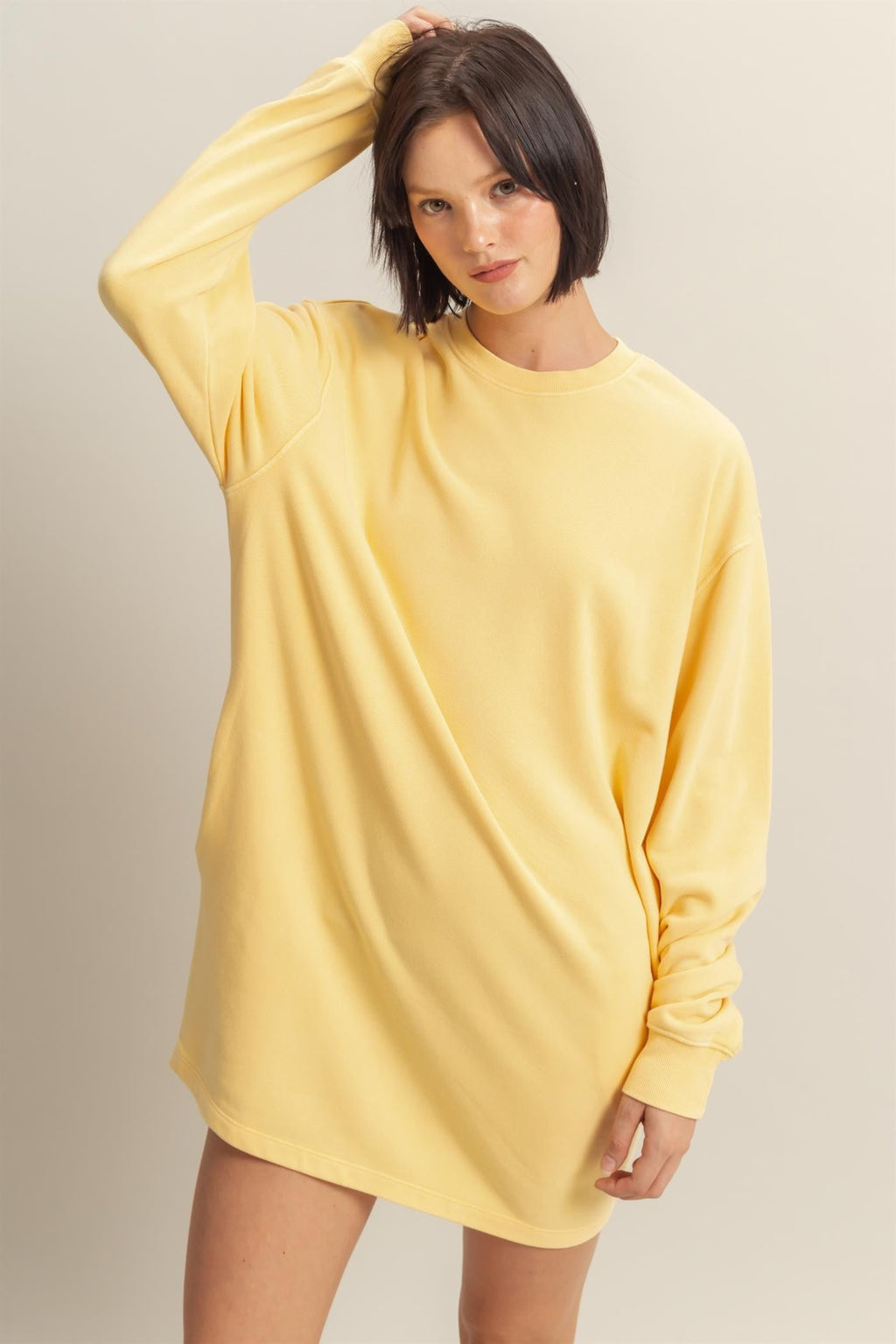 A model wearing a bright yellow long sleeve oversized sweatshirt mini dress with a crew neck, styled with yellow checkered slip-on shoes.