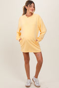 A pregnant woman wearing an oversized yellow long sleeve sweatshirt mini dress with side pockets.