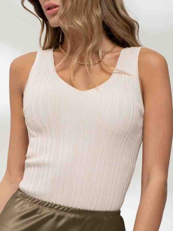 A woman wearing a minimalist oatmeal-colored V-neck sweater knit tank top in a casual setting.