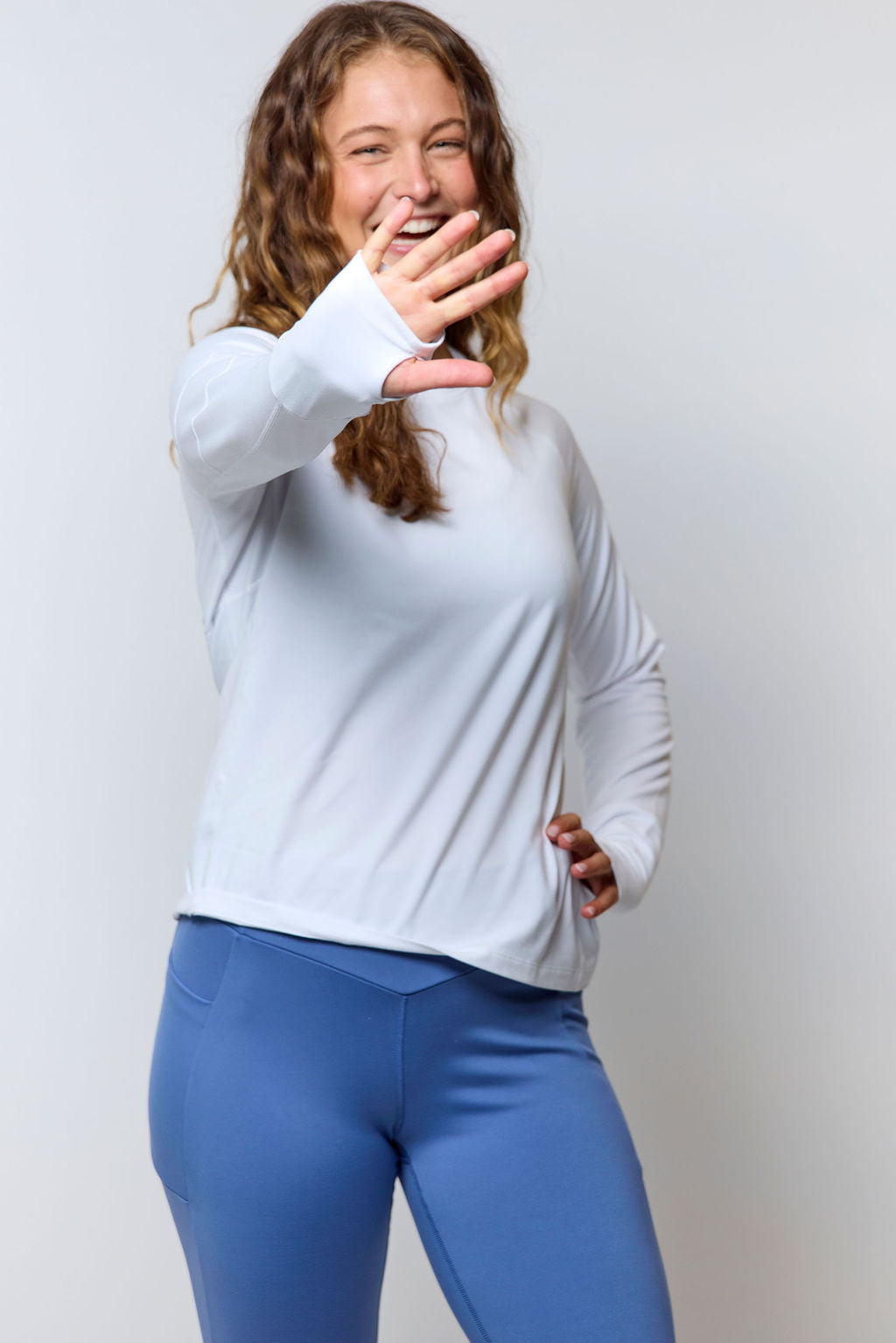 Woman wearing a white long sleeve athletic top with thumbholes, paired with blue performance leggings