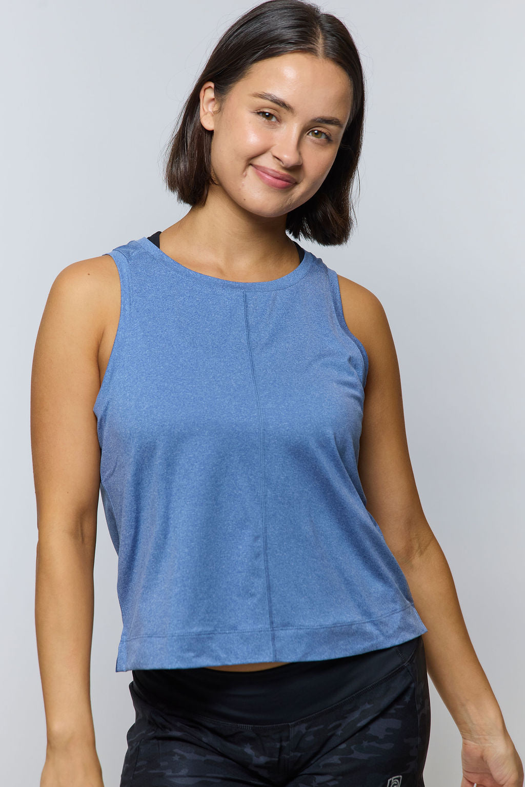 A woman wearing a blue boxy crop tank top with a crew neckline in an athletic setting.