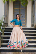 Model wearing an off-white Tussar silk lehenga choli with vibrant lotus floral prints and teal accents