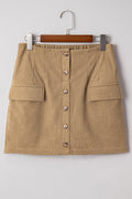 Tan corduroy mini skirt with button front detail and faux pockets hanging on a wooden hanger against a neutral background