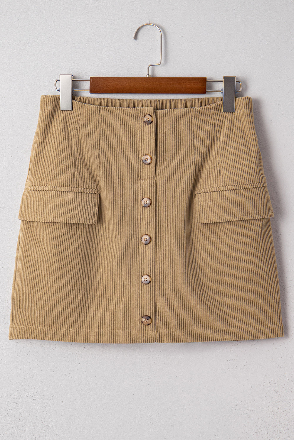 Tan corduroy mini skirt with button front detail and faux pockets hanging on a wooden hanger against a neutral background