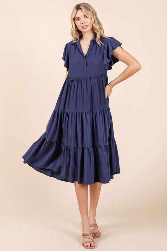 Woman wearing a navy blue collared midi dress with ruffle sleeves and tiered skirt