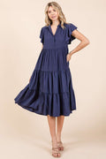 Woman wearing a navy blue collared midi dress with ruffle sleeves and tiered skirt