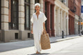 Model wearing a loose-fitting white maxi dress with batwing sleeves and a casual collar, styled with a straw tote bag.