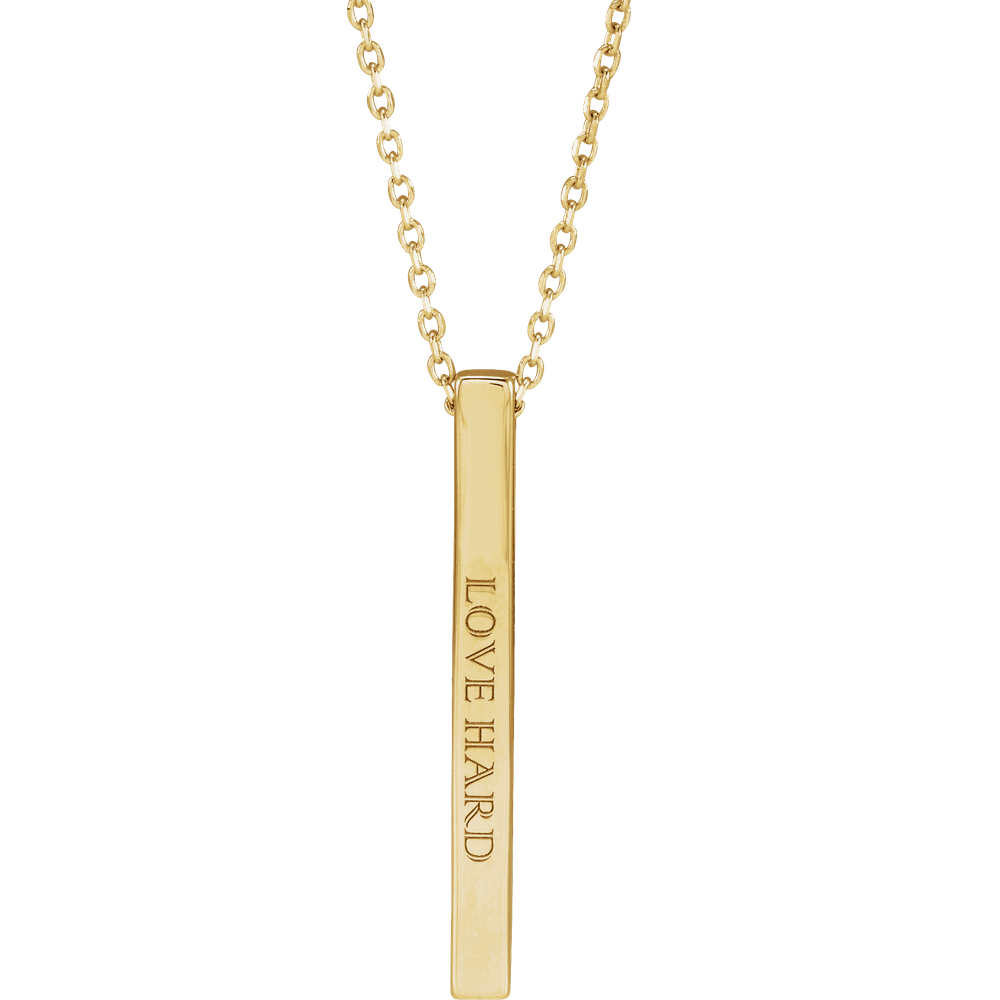 Amélie 14K yellow gold four-sided engravable bar necklace resting on a neutral background