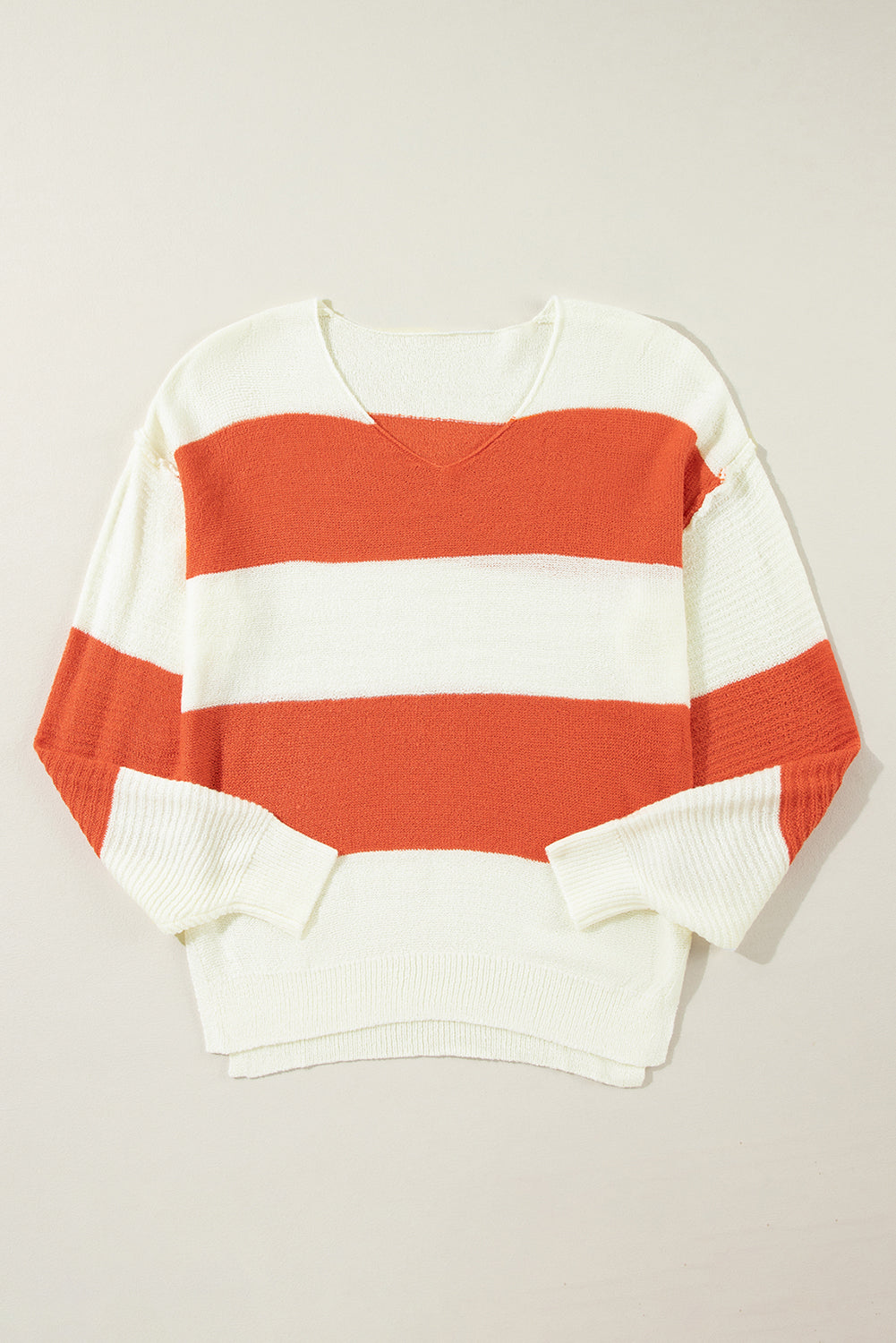 Flat lay of a white and orange striped V-neck sweater with drop shoulders and bubble sleeves, showcasing its knit texture.