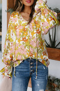A woman wearing a long-sleeved, smocked-cuff blouse with a yellow and pink floral pattern against a cream background, styled with blue jeans.