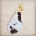 A teardrop-shaped brindle cowhide leather keychain featuring hair-on-hide texture and a gold-tone clasp on a light wooden background.