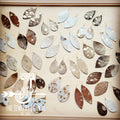 A variety of metallic hair-on-hide leather teardrop earrings displayed on a wooden board.