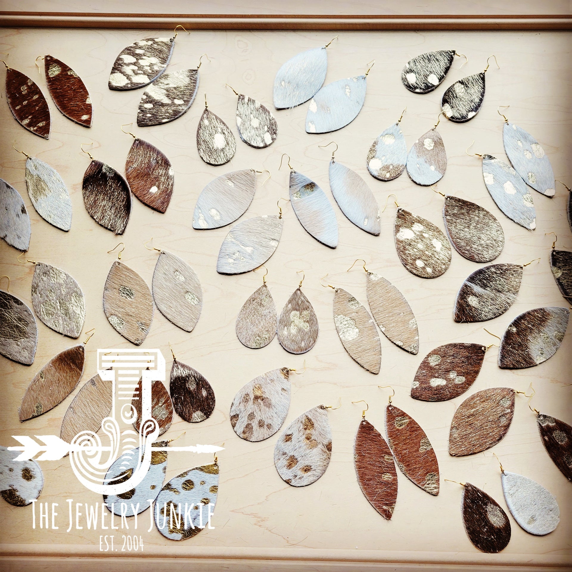 A variety of metallic hair-on-hide leather teardrop earrings displayed on a wooden board.