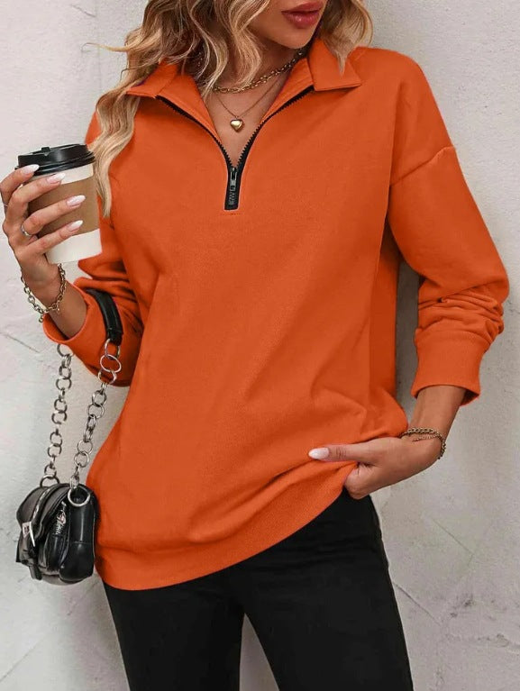 Person wearing an orange long-sleeve top with a zipper, holding a coffee cup and a black handbag.