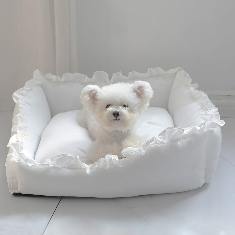 A small white puppy resting in an elegant white ruffled princess dog bed.