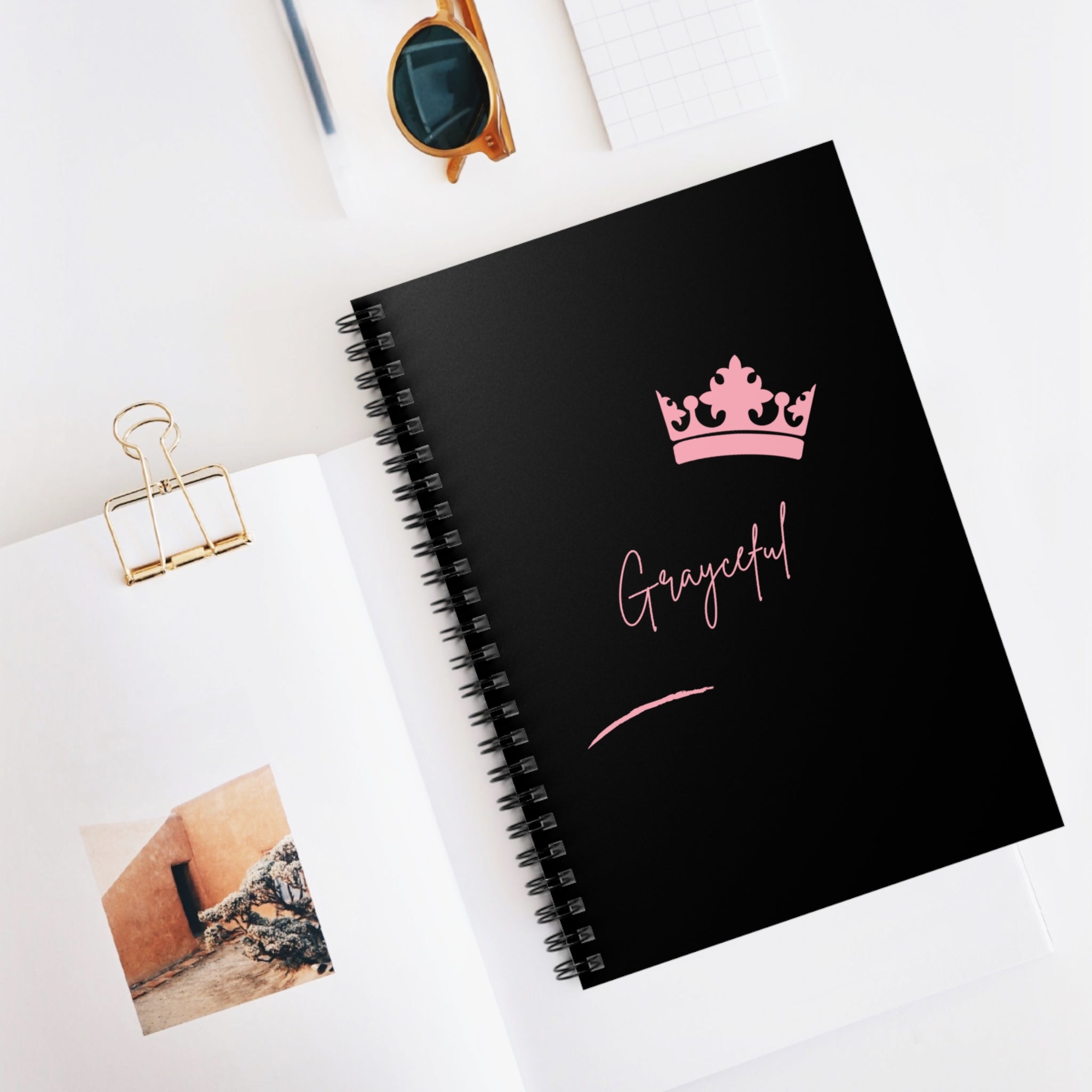 Minimalist spiral notebook featuring a black cover and pale pink graphic accents on a clean desk surface.
