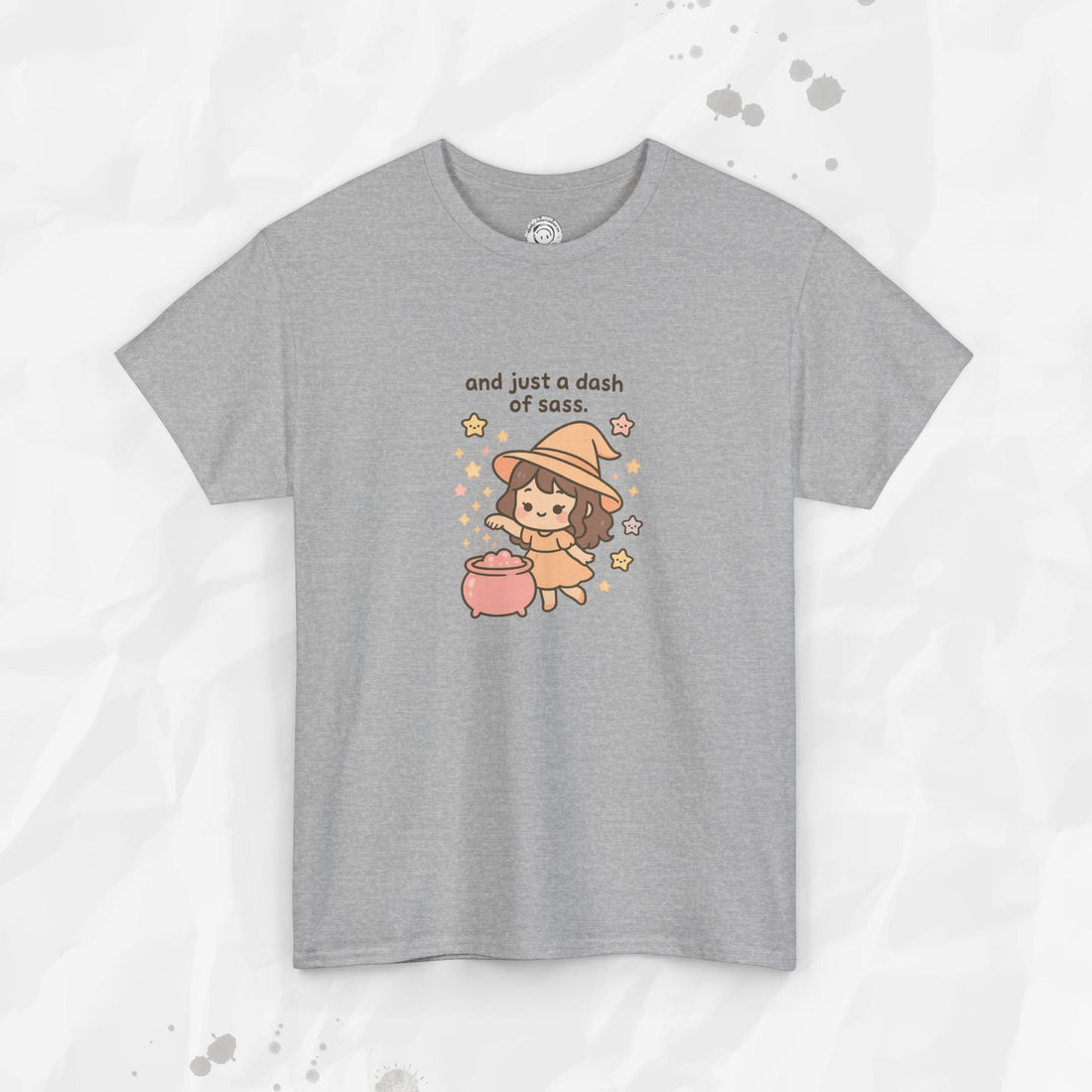A pastel pink and grey graphic t-shirt featuring a cute cartoon witch brewing a potion with the text And just a dash of sass.