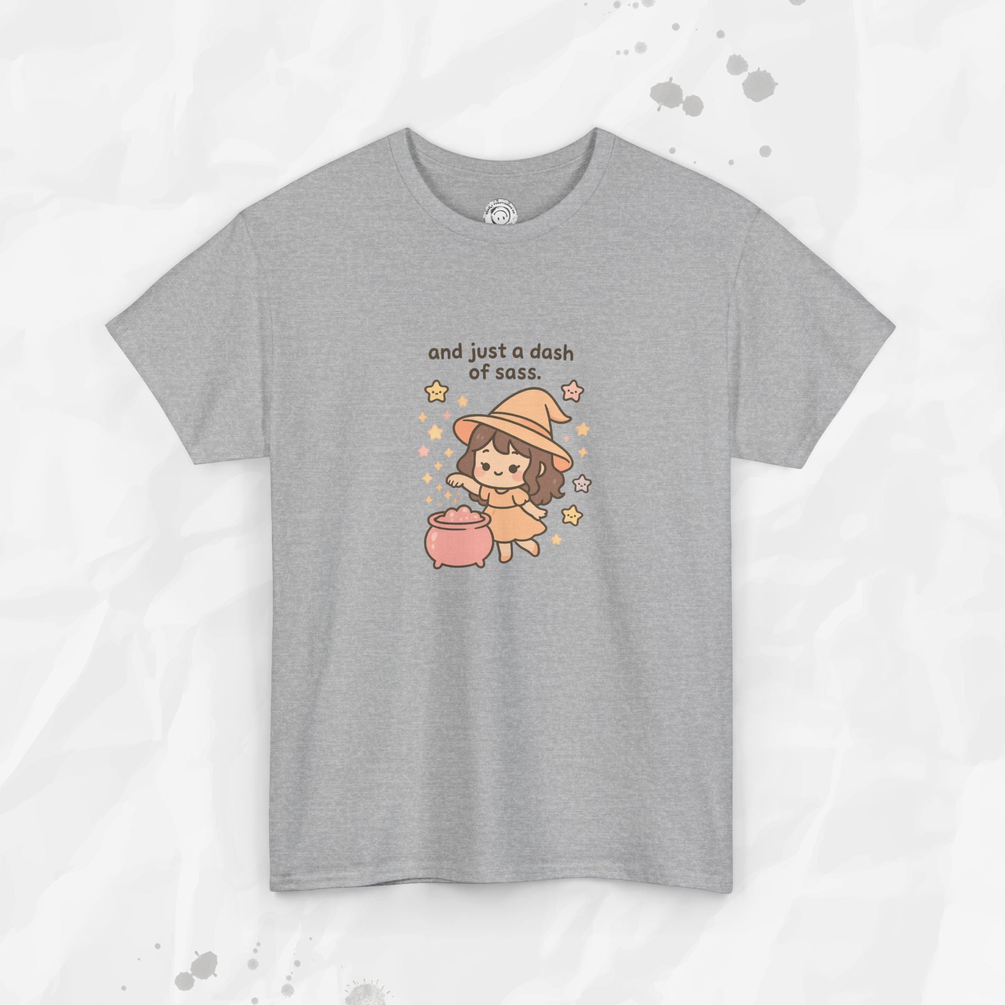 A pastel pink and grey graphic t-shirt featuring a cute cartoon witch brewing a potion with the text And just a dash of sass.