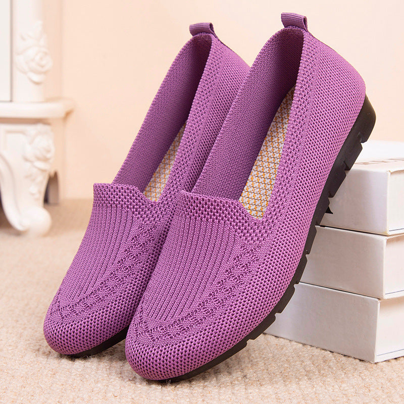 A pair of purple knit slip-on loafers shown against a white surface, featuring a mesh texture and flexible construction.