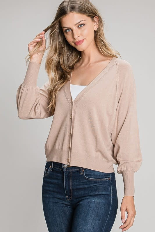 A woman wearing a relaxed fit, oatmeal-colored knit cardigan with balloon sleeves and a V-neckline button closure.